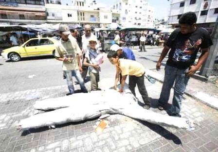 فلسطينيون ينظرون بكل حزن إلى بقايا تمثال الجندي المجهول على الأرض في غزة  الذي كان يعتبر رمزاً للنضال الفلسطيني ضد إسرائيل بينما تعتبره حماس صنماً وشركاًً بالله يستحق التحطيم