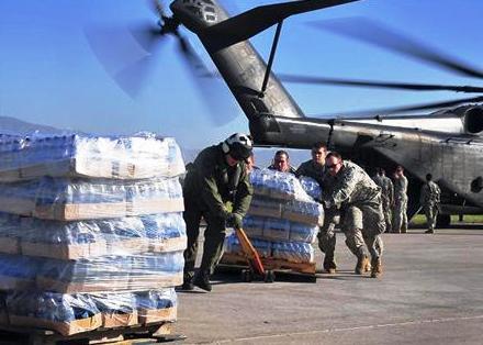 أفراد من الجيش الأمريكي يساعدون طاقم طائرة هليكوبتر تابعة لسلاح البحرية في تفريغ إمدادات غذائية بمطار بورت او برنس في هايتي يوم أول أمس الجمعة.