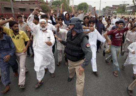 شرطي باكستاني يحاول تهدئة محتجين على تفجير المزار في لاهور بباكستان أمس الأول  الجمعة.