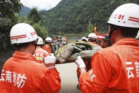 عمال انقاذ يحملون جثة شخص قتل في انهيار طيني بقرية في اقليم يونان الصيني أمس