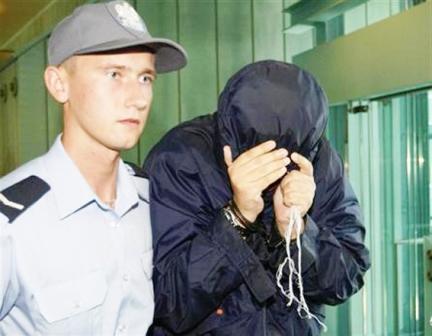 يوري برودسكي يغطي وجهه وهو يسير الى جانب شرطي بولندي في محكمة بوارسو أمس الخميس.