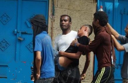 صورة رقم 1 :  الشاب أحمد درويش مرتديا الفانيلة البنية مسعفا أحد الجرحى قبل بضع دقائق من مقتله